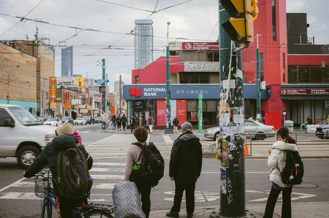 Diverse pedestrians waiting to cross a busy downtown Toronto intersection