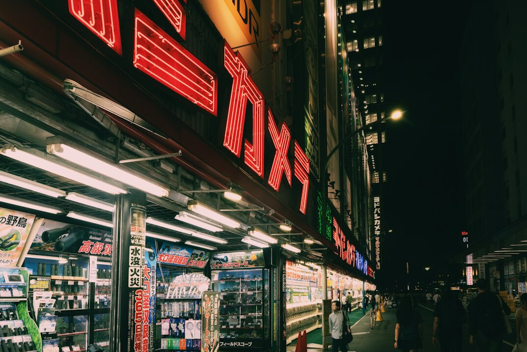 Evening view of a city street with pedestrians and lit storefronts
